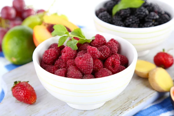 Raspberries and blackberry in small bowls on board on napkin isolated on white — Stock Photo, Image