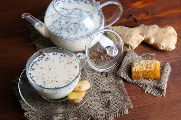 Teapot and cup of tea with milk and spices on sackcloth of wooden table