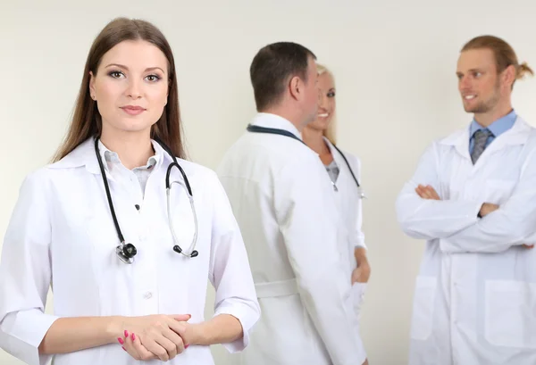 Dokter staan voor collega's op grijze achtergrond — Stockfoto