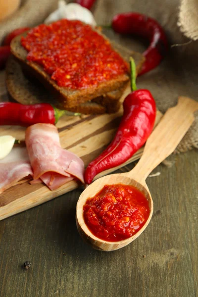 Composition with salsa sauce on bread,, red hot chili peppers and garlic, on sackcloth, on wooden background — Stock Photo, Image