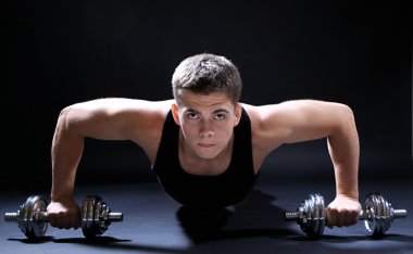 yakışıklı genç kaslı sporcu, koyu arka plan üzerinde egzersiz halter ile yürütmek