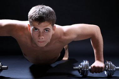 yakışıklı genç kaslı sporcu, koyu arka plan üzerinde egzersiz halter ile yürütmek