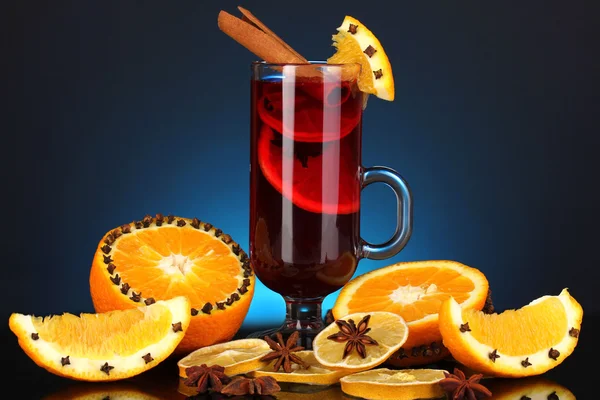 Duftender Glühwein im Glas mit Gewürzen und Orangen auf blauem Hintergrund — Stockfoto