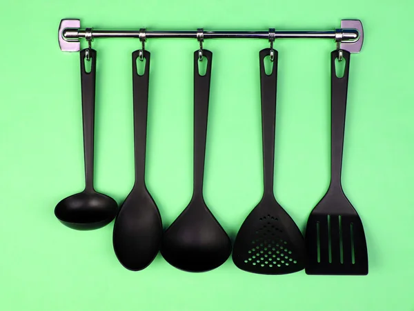 Black kitchen utensils on silver hooks, on green background — Stock Photo, Image