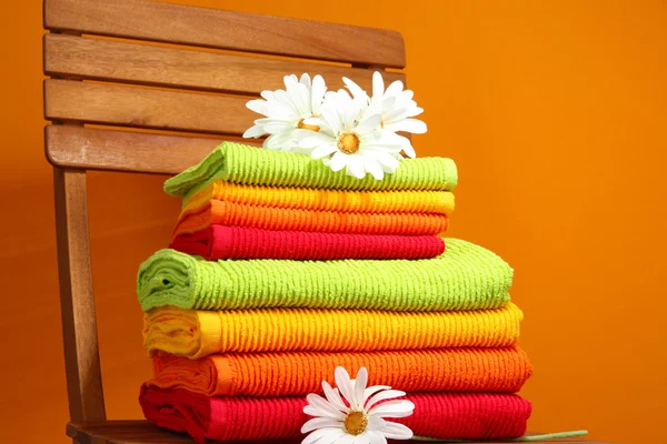 Ručníky a květiny na dřevěné židli na oranžovém pozadí — Stock fotografie
