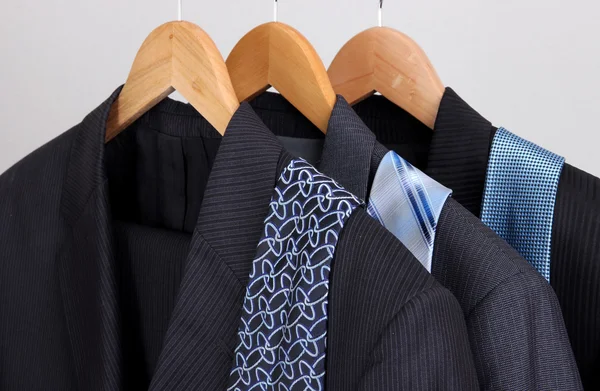 Garnitury i krawaty na wieszaki na szarym tle — Zdjęcie stockowe