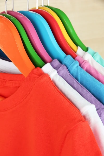 Różne koszulki na wieszakach kolorowe na jasnym tle — Zdjęcie stockowe