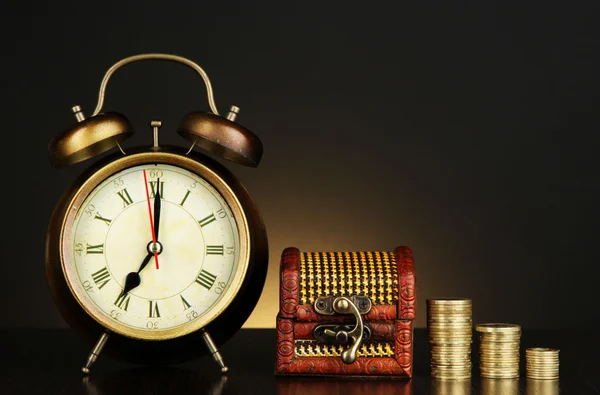 Horloge antique et pièces de monnaie sur table en bois sur fond de couleur sombre — Photo