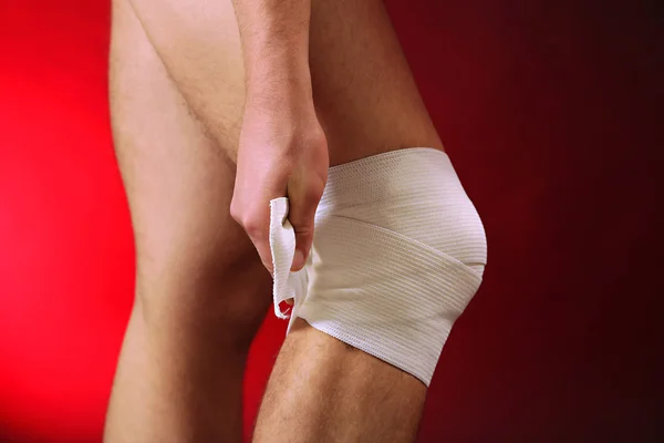 Young man with elastic bandage on knee, on red background — Stock Photo, Image