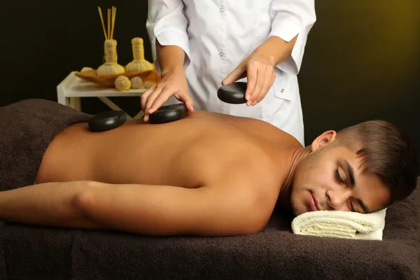 Jonge man met stenen massage in de spa salon — Stockfoto