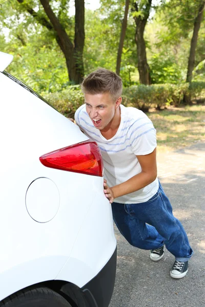 Young man pushing broken down car — Stock Photo, Image