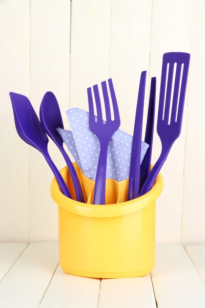 Utensilios de cocina de plástico en taza sobre mesa de madera — Foto de Stock