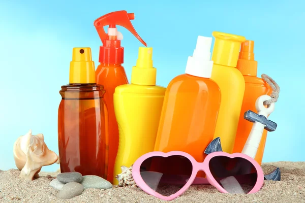 Botellas con crema bronceadora y gafas de sol, sobre fondo azul —  Fotos de Stock