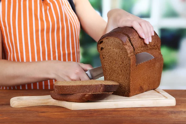 Cutting bread on wooden board on wooden table on window background — Stock Photo, Image