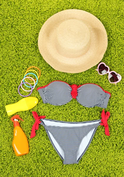 Swimsuit and beach items on green background — Stock Photo, Image