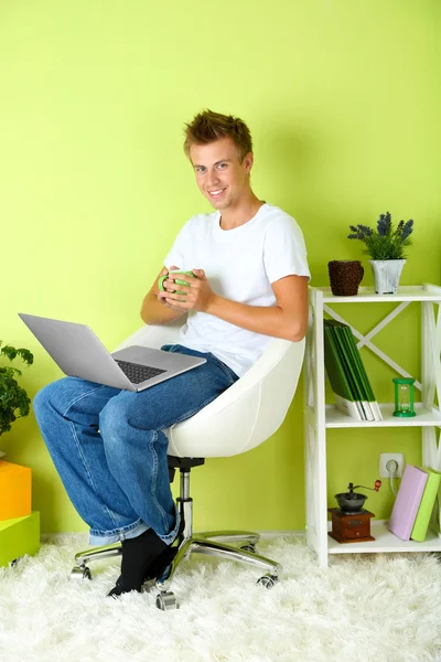 Jeune homme relaxant avec ordinateur portable dans le fauteuil, sur le fond intérieur de la maison — Photo