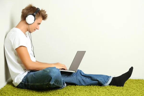 Młody człowiek, relaksując się na dywan i słuchanie muzyki, na tle szarej ściany — Zdjęcie stockowe