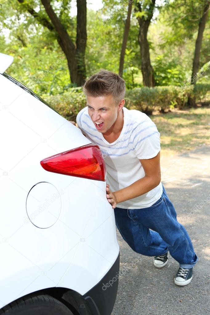Young man pushing broken down car