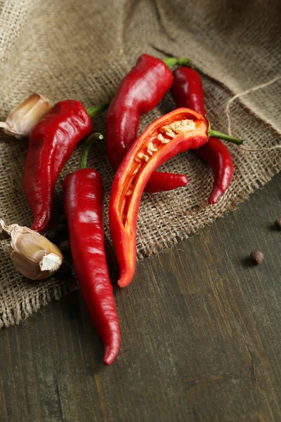 Red hot chili peppers en knoflook, op rouwgewaad, op houten achtergrond — Stockfoto