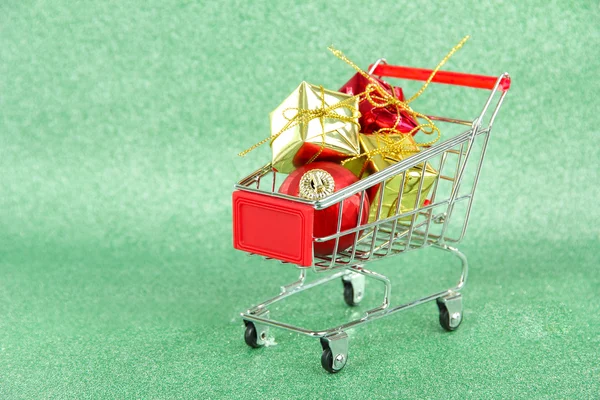 Christmas gifts in shopping trolley, on green shiny background — Stock Photo, Image
