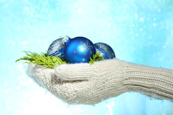 Mãos femininas em mitenes bolas de árvore de Natal, em fundo de cor — Fotografia de Stock