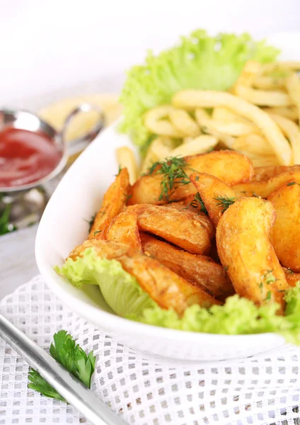 French fries and home potatoes on plate on board on napkin on wooden table — Stock Photo, Image