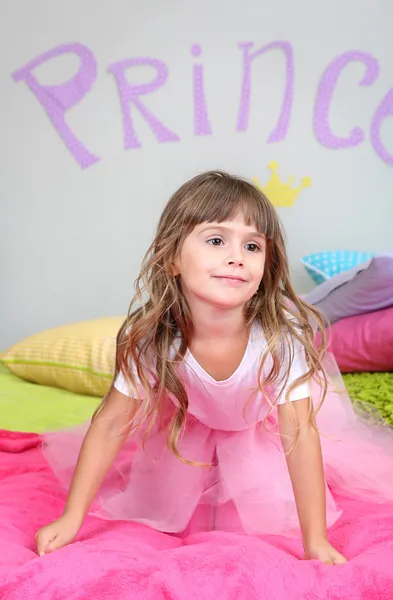 Menina pulando na cama no quarto no fundo da parede cinza — Fotografia de Stock