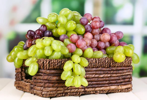 Uvas verdes e roxas maduras em cesta sobre mesa de madeira sobre fundo natural — Fotografia de Stock