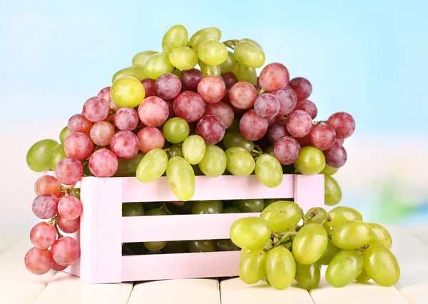 Ripe green and purple grapes in wooden box on wooden table on natural background