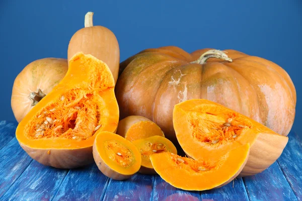 Ripe cut pumpkins on wooden table on blue background — Stock Photo, Image
