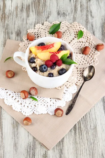 Oatmeal in cup with berries on napkins on wooden table — Stock Photo, Image