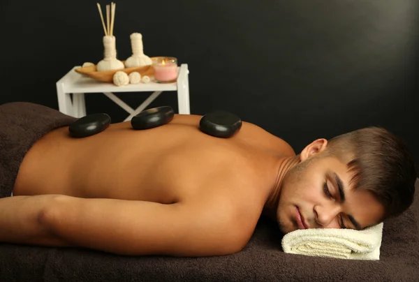Giovane uomo rilassante con pietre calde sulla schiena prima del massaggio — Foto Stock