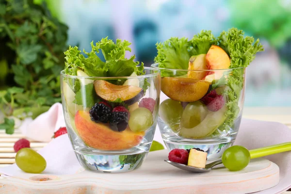 Fruit salad in glasses, on wooden table, on bright background — Stock Photo, Image