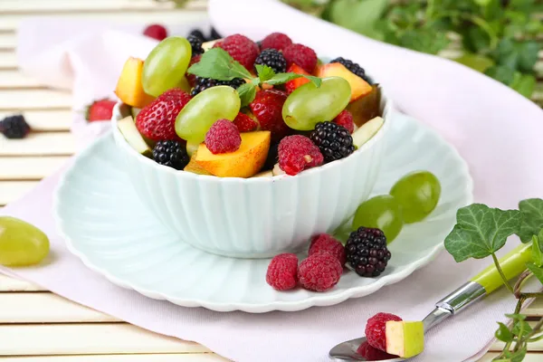 Fruit salad in bowl, on wooden table, on bright background — Stock Photo, Image