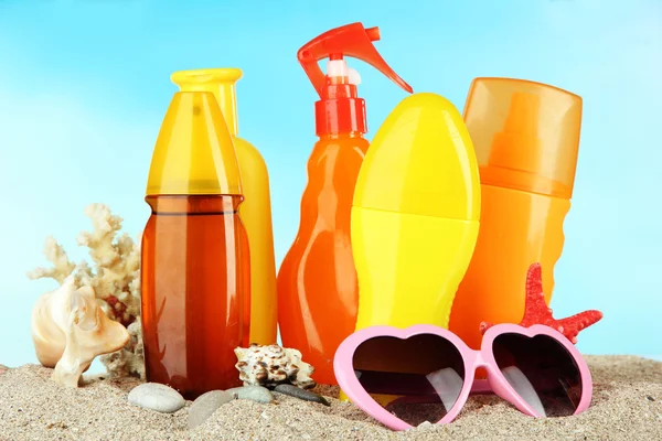 Flaskor med solbränna grädde och solglasögon, på blå bakgrund — Stockfoto