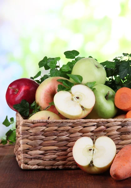 Manzanas dulces y zanahorias en cesta sobre mesa de madera sobre fondo natural — Foto de Stock