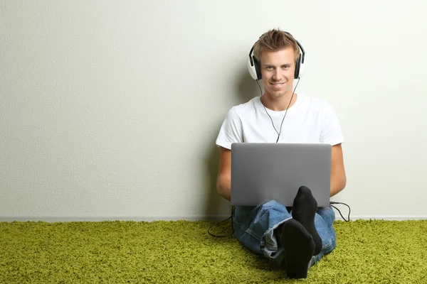 Hombre joven relajándose en la alfombra y escuchando música, sobre fondo gris de la pared — Foto de Stock