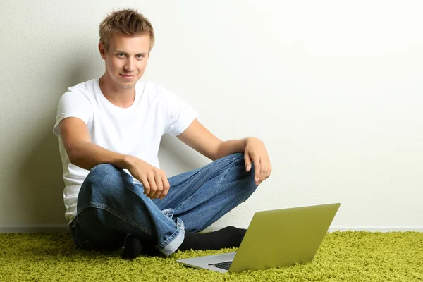 Jovem relaxante no tapete com laptop, no fundo da parede cinza — Fotografia de Stock