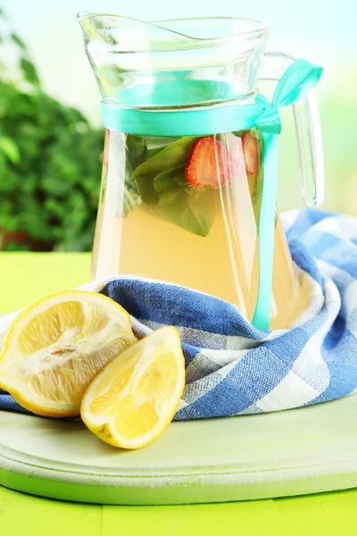 Basil lemonade with strawberry in jug and glass, on wooden table, on bright background — Stock Photo, Image