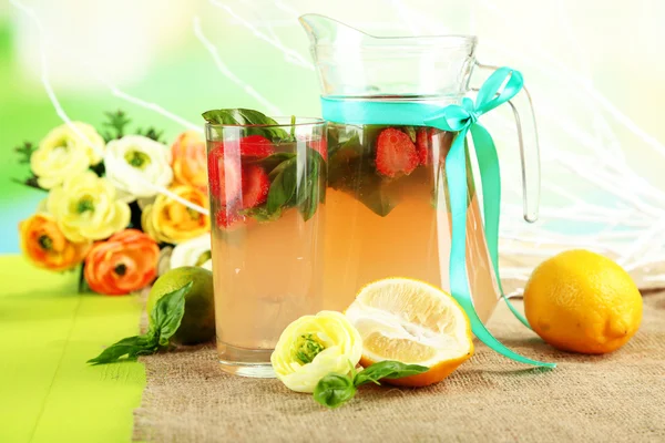 Basil lemonade with strawberry in jug and glass, on wooden table, on bright background — Stock Photo, Image