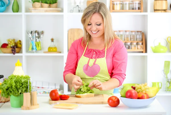 Happy smiling woman in kitchen preparing sandwich — Stock Photo, Image
