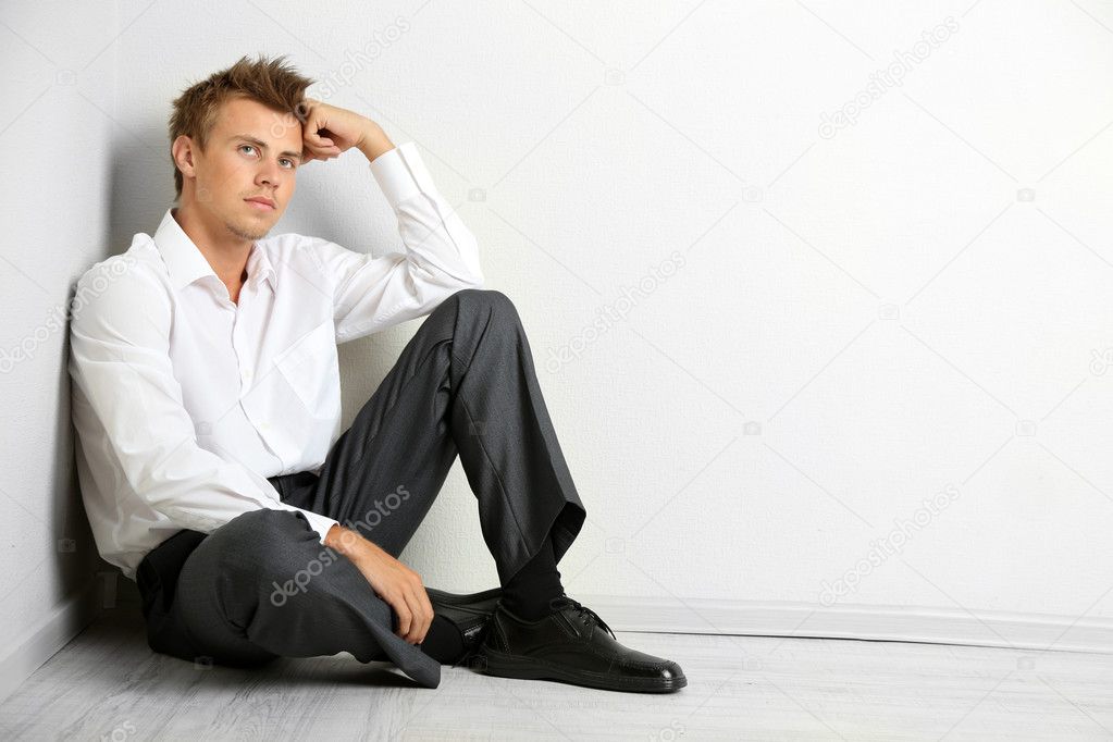 Young businessman sitting on floor, on gray wall background