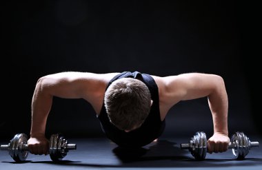 yakışıklı genç kaslı sporcu, koyu arka plan üzerinde egzersiz halter ile yürütmek