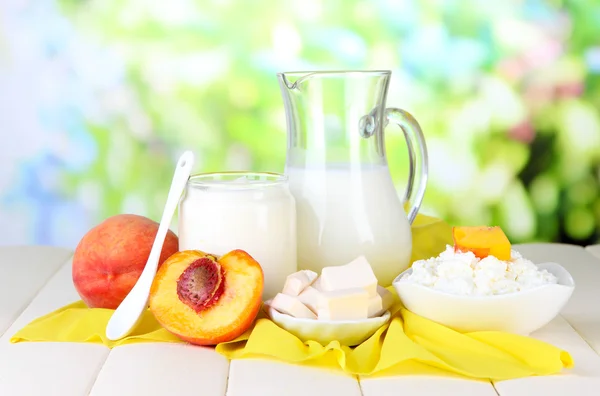 Frische Milchprodukte mit Pfirsichen auf Holztisch vor natürlichem Hintergrund — Stockfoto