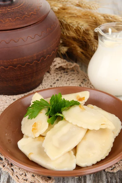 Tasty dumplings with fried onion on brown plate, on wooden background — Stock Photo, Image