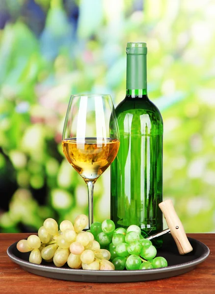 Botella de vino y copa de vino en bandeja, sobre fondo brillante — Foto de Stock