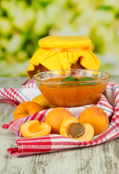 Marillenmarmelade in Glasschale und frischen Aprikosen, auf Holztisch, auf hellem Hintergrund — Stockfoto