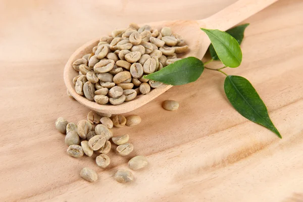 Granos de café verdes en cuchara y hojas sobre fondo de madera — Foto de Stock