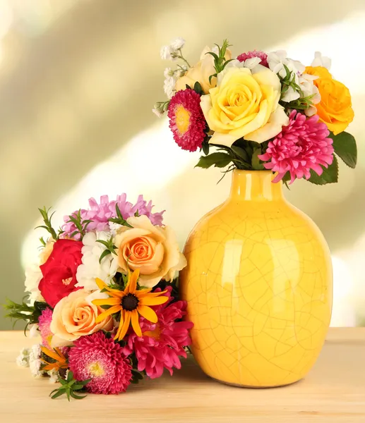 Beautiful bouquet of bright flowers in color vase, on wooden table, on bright background — Stock Photo, Image