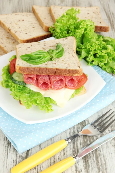 Composição com suco de frutas e saboroso sanduíche com salsicha de salame e legumes em guardanapo de cor, em fundo de mesa de madeira — Fotografia de Stock